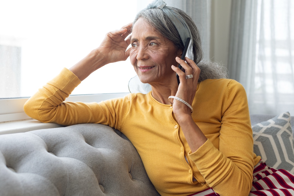An older woman sitting at home, smiling as she talks on the telephone.